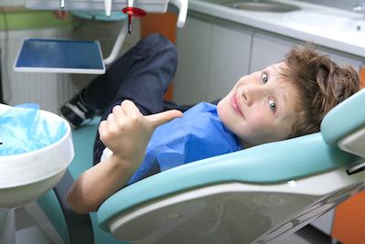 young boy smiling in dental chair and giving the dentist a thumbs up