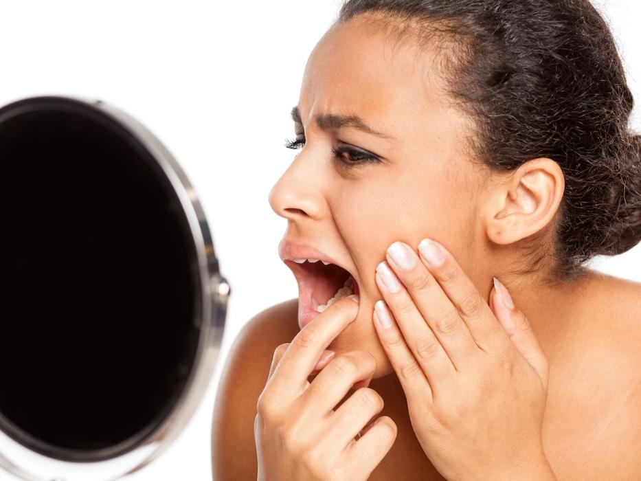 woman checking her tooth in a mirror during a dental emergency