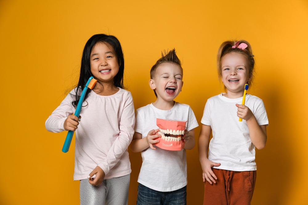 three young kids smiling and holding a toothbrush