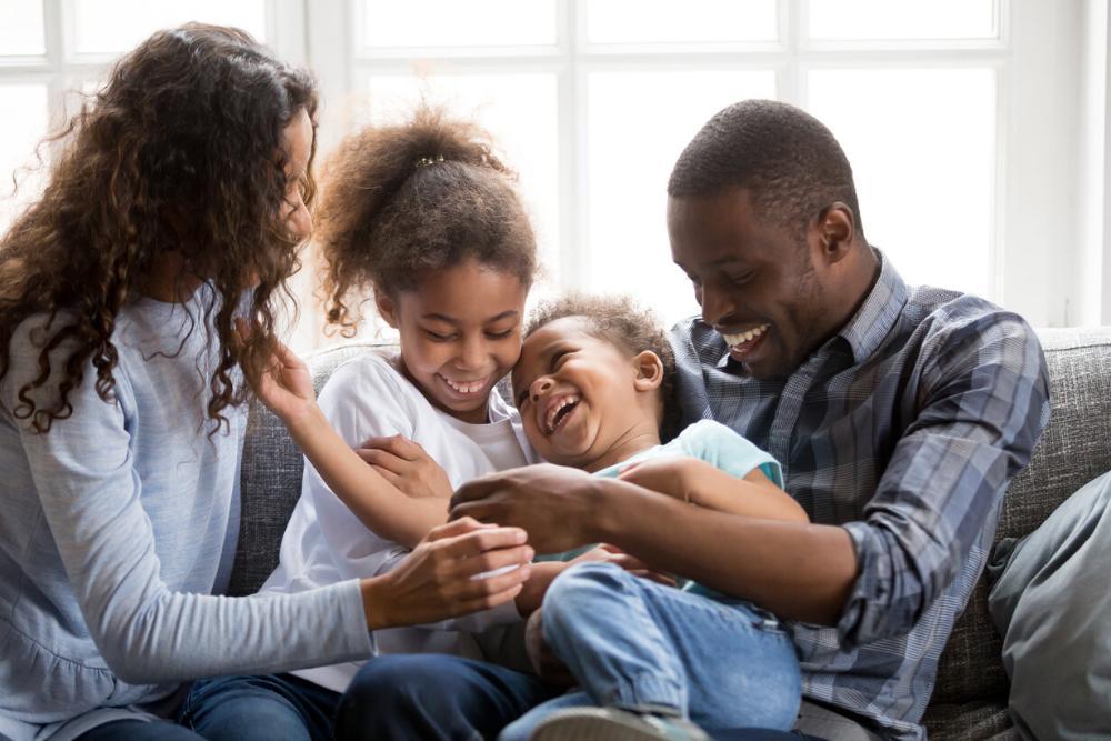 family of four laughing and playing on the couch