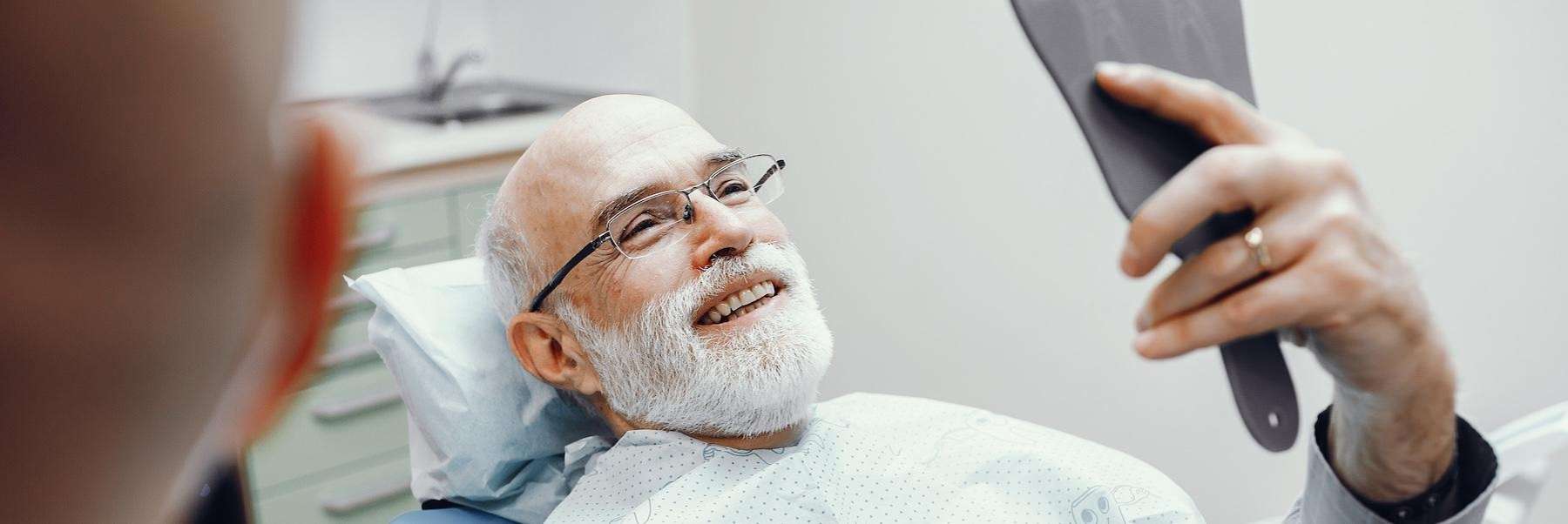 north york man smiling into dental mirror after dental bridge