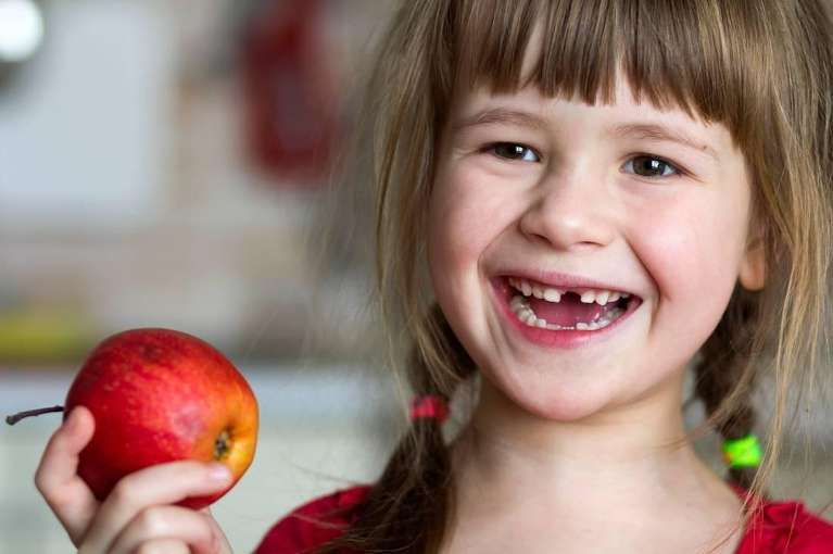 young girl missing her front tooth and holding an apple