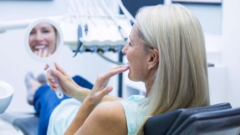 north york woman looking at dental mirror after getting dental implants
